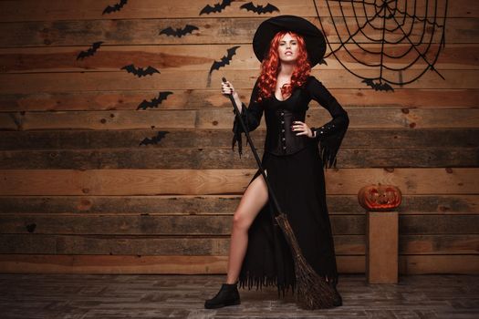 Halloween witch concept - Full-length Happy Halloween red hair Witch holding posing with magic broomstick over old wooden studio background