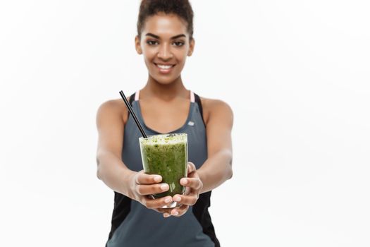 Healthy and Fitness concept - Beautiful American African lady in fitness clothing drinking healthy vegetable drink. Isolated on white background