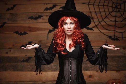 Halloween witch concept - Happy Halloween red hair Witch holding posing with shocked face over old wooden studio background