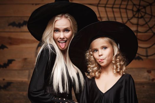Halloween Concept - Closeup beautiful caucasian mother and her daughter in witch costumes celebrating Halloween posing with curved pumpkins over bats