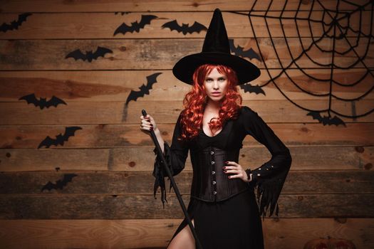 Halloween witch concept - Happy Halloween red hair Witch holding posing with magic broomstick over old wooden studio background