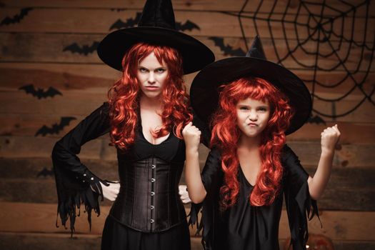 Halloween Concept - Beautiful caucasian mother and her daughter with long red hair in witch costumes witch cheerful fighting facial expression