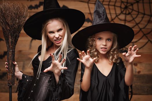 Halloween Concept - Closeup beautiful caucasian mother and her daughter in witch costumes celebrating Halloween posing with curved pumpkins over bats