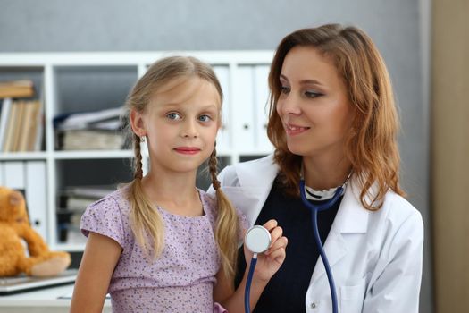 Portrait of pediatrician doctor with child on lap, kid play with stethoscope tool, happy kid on appointment, health. Medicine, childhood, checkup concept