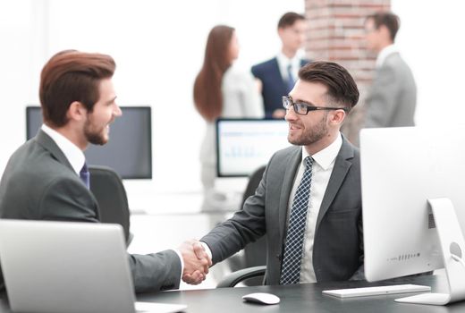 Two managers in suits shaking hands at business meeting in office