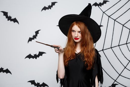 Halloween Concept - Beautiful Witch playing with magic stick on grey background