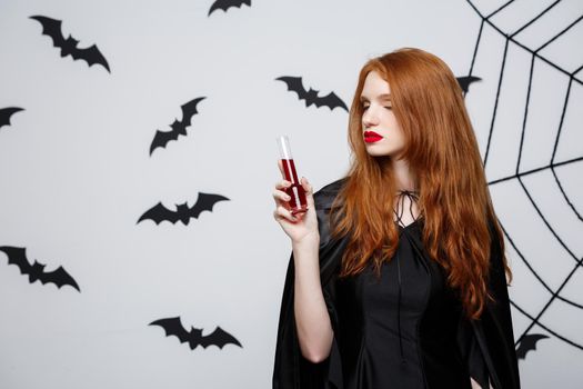 Halloween witch concept - Happy Halloween Witch drinking blood over dark grey studio background with bat and spider web