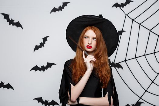 Halloween Concept - Beautiful Witch playing with magic stick on grey background