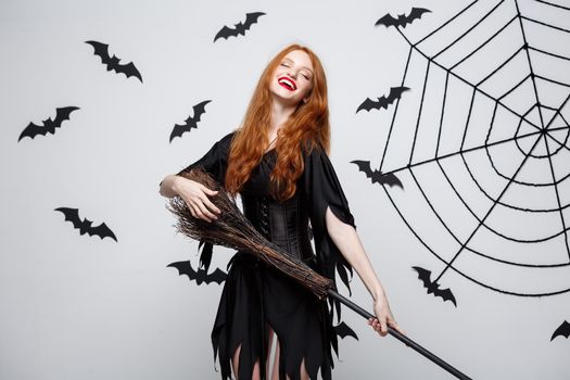 Halloween Concept - Happy elegant witch enjoy playing with broomstick halloween party over grey background