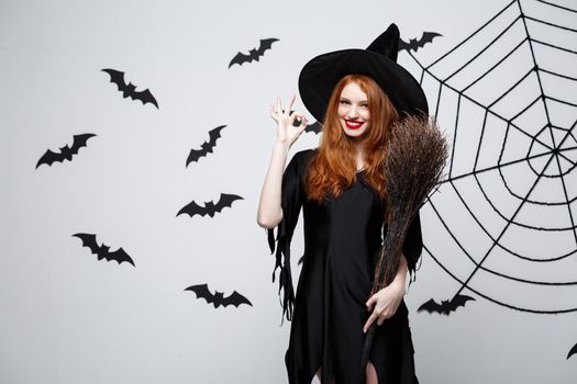 Halloween Concept - Happy elegant witch with broomstick halloween doing OK sign with finger