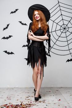 Halloween witch concept - Full-length of Happy Halloween Witch holding posing over dark grey studio background with bat and spider web