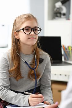 Portrait of young child wants to be doctor, write advices on paper, wear stethoscope equipment on neck. Education, knowledge, future medical worker concept