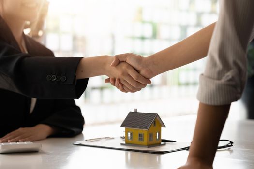 Real estate broker and customer shaking hands after signing a contract: real estate, home loan and insurance concept.