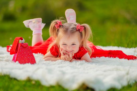 a girl in a red dress lies on a white blanket that is laid on the lawn