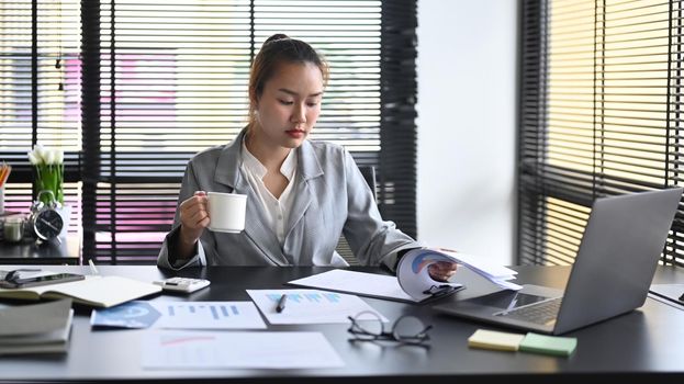Professional businesswoman drinking coffee and working at modern office.