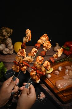 Woman hands holding grilled skewers of chicken, bell peppers, tomatoes, onion. Close up.