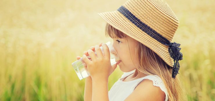 A child drinks water on the background of the field. Selective focus.