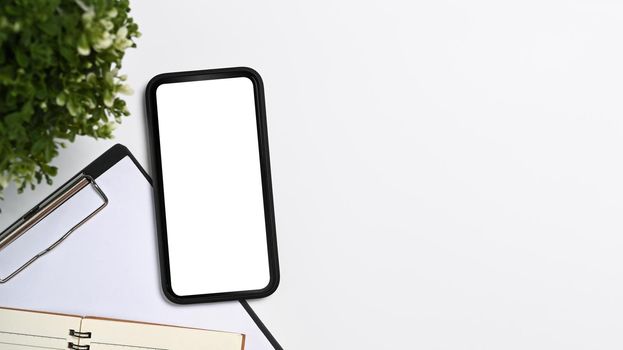 Smart phone, clipboard, and houseplant on white table. Top view with copy space.