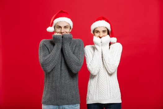 Christmas Concept - Portrait of smiling mouth tapping couple looking in camera with opened eyes over red studio background.
