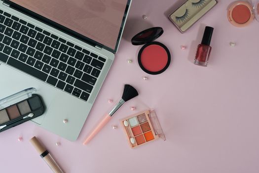 Top view feminine workspace with laptop and cosmetics on pink background.