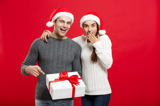 Christmas Concept - portrait young couple in Christmas sweater pointing finger gesture to gifts.