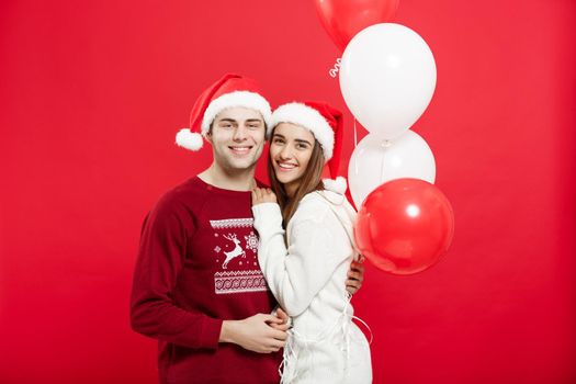 Christmas concept - Portrait of a romantic young couple with christmas balloon over red studio background.