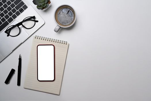 Top view mobile phone, laptop, notebook, glasses and coffee cup on white table. Minimal workplace, copy space.