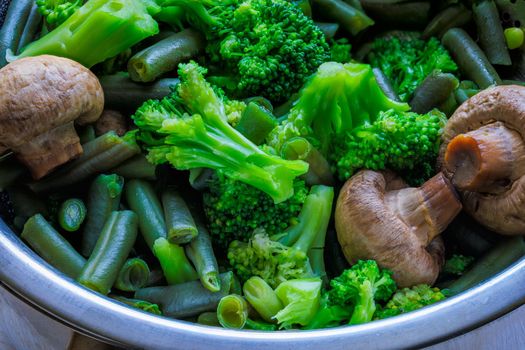 boiled green vegetables - broccoli, green beans and champignon mushrooms in stainless steel colander - full-frame closeup
