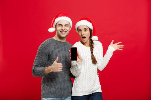 Christmas concept - Happy young couple in christmas sweaters showing thump up gesture with mobile phone.