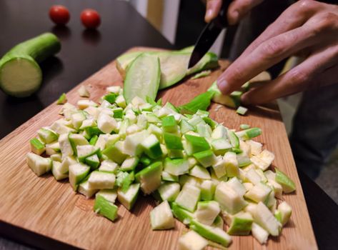 Close up Hands of young man cut with knife into slices of zucchini cucumber on wooden cutting board.