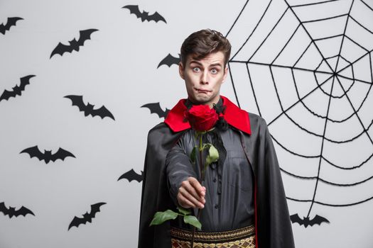 Vampire Halloween Concept - Portrait of handsome caucasian Vampire holding red beautiful rose