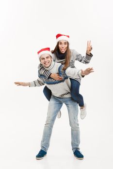 Christmas Concept - Young happy couple in sweaters enjoying piggyback ride isolated on white grey background.