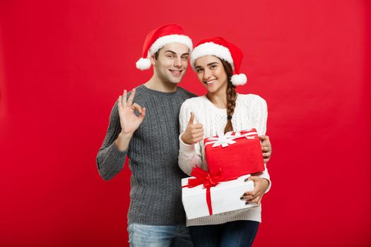 Christmas Concept - portrait young couple in Christmas sweater showing ok gesture with gifts.