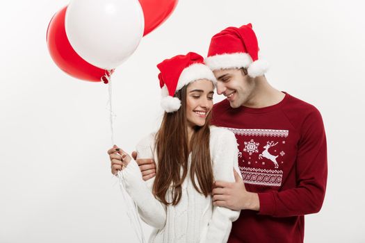 Christmas Concept - Young girlfriend holding balloon is hugging and playing with her boyfriend doing a surprise on Christmas.