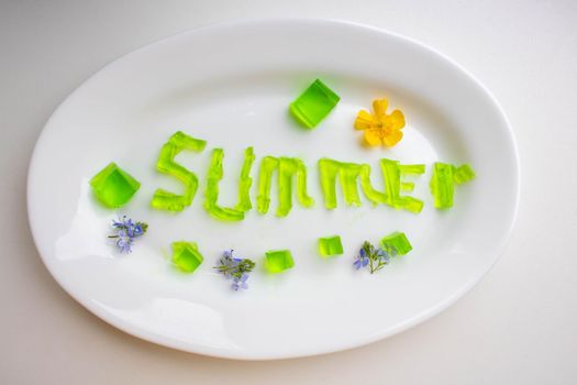 The word summer is made of green jelly cubes on a white plate.