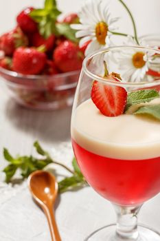 Cherry and milk jelly with strawberry piece in the glass topped mint leaves and strawberries in a bowl with chamomiles on the background