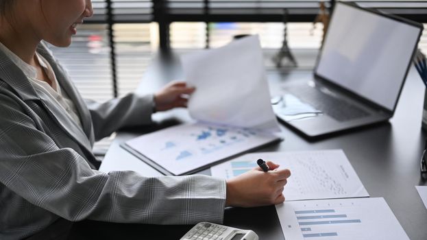Concentrated female director reviewing financial charts and graphs data in document at office desk.