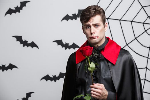 Vampire Halloween Concept - Portrait of handsome caucasian Vampire holding red beautiful rose