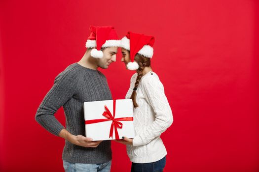 Christmas Concept - isolated lovely young couple holding tight with white gift over red background.