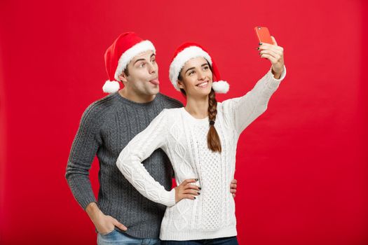 Christmas Concept - Young attractive couple taking a selfie by mobile phone celebrating in Christmas day.