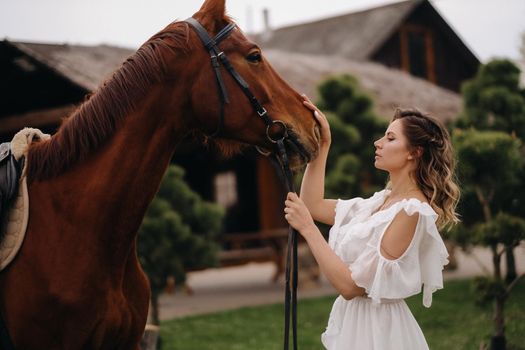 Beautiful girl in a white sundress next to a horse on an old ranch.