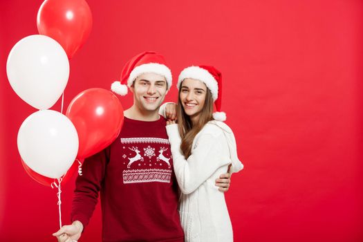 Christmas concept - Portrait of a romantic young couple with christmas balloon over red studio background.