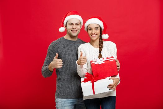 Christmas Concept - portrait young couple in Christmas sweater showing thump up with gifts.