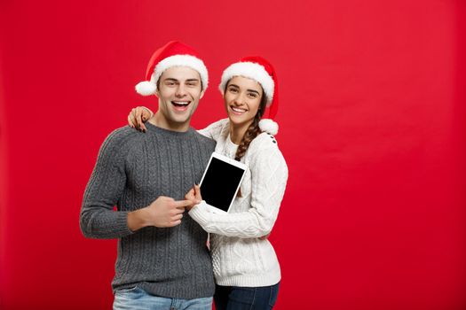 Christmas concept - Happy young couple in christmas sweaters holding digital tablet.