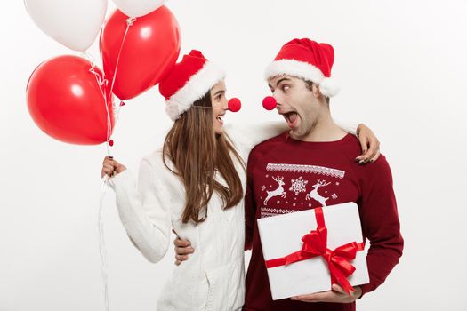 Christmas Concept - Young caucasian couple holding gifts,champagne and balloon making funny face on Christmas.