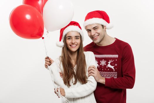 Christmas Concept - Young girlfriend holding balloon is hugging and playing with her boyfriend doing a surprise on Christmas.