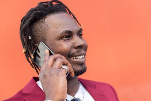 portrait of a stylish black businessman in suit smiling and talking on phone in front of red background, copy space for text, concept of technology and communication