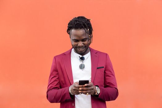 stylish black businessman in suit typing a message on his smart phone in front of a red background, copy space for text, concept of technology and communication