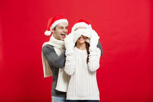 Christmas concept - Portrait of a romantic young boyfriend surprising girlfriend over red studio background.