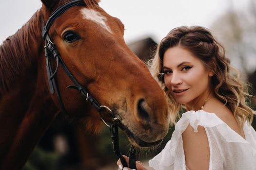 Beautiful girl in a white sundress next to a horse on an old ranch.